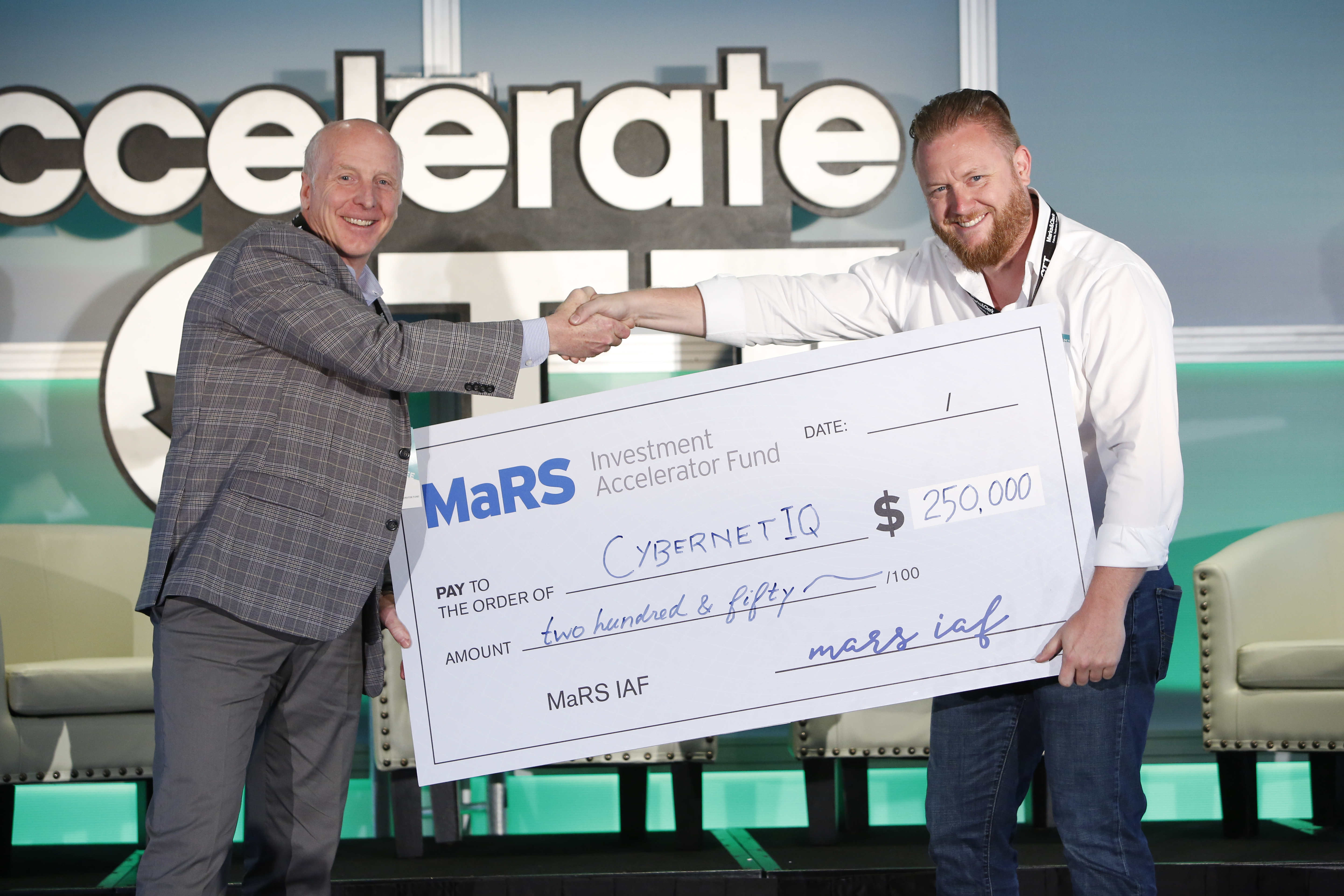 Two men shaking hands while holding a giant cheque.