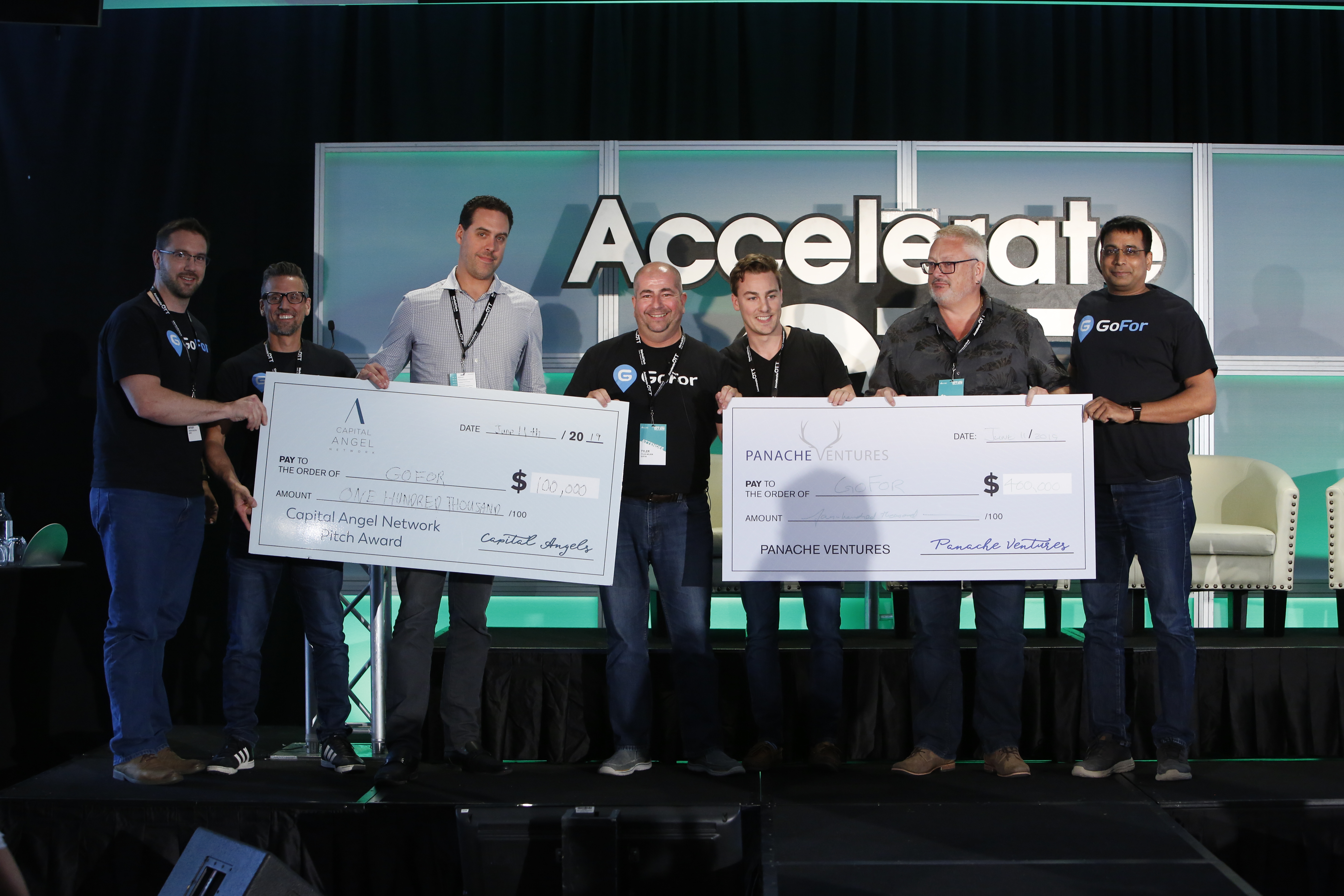 Winners of PitchFest holding giant cheques. GoFor wins PitchFest at AccelerateOTT 2019, held at the National Arts Centre in Ottawa, Ontario, Canada on June 11, 2019. Photo by David Kawai for Invest Ottawa.