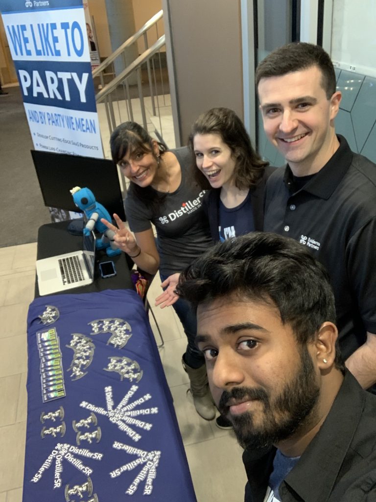 Evidence Partners team members smiling for a selfie in front of their booth at a career fair.