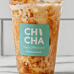 A cup of chicha - topped with cinnamon - the logo of the company is added to the front of the cup.