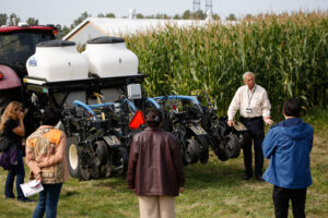 An individual presenting tech farming solutions to participants at an outdoor demonstration event.