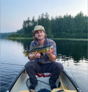 Founder of ReCast Fishing holds up a fish while out on a lake in a boat. 