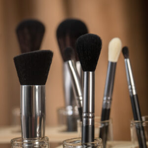 A photo of makeup brushes in glass containers standing upright. 