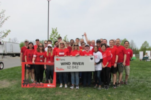 A team picture of the Wind River team standing behind a large charity cheque at an outdoor event. 